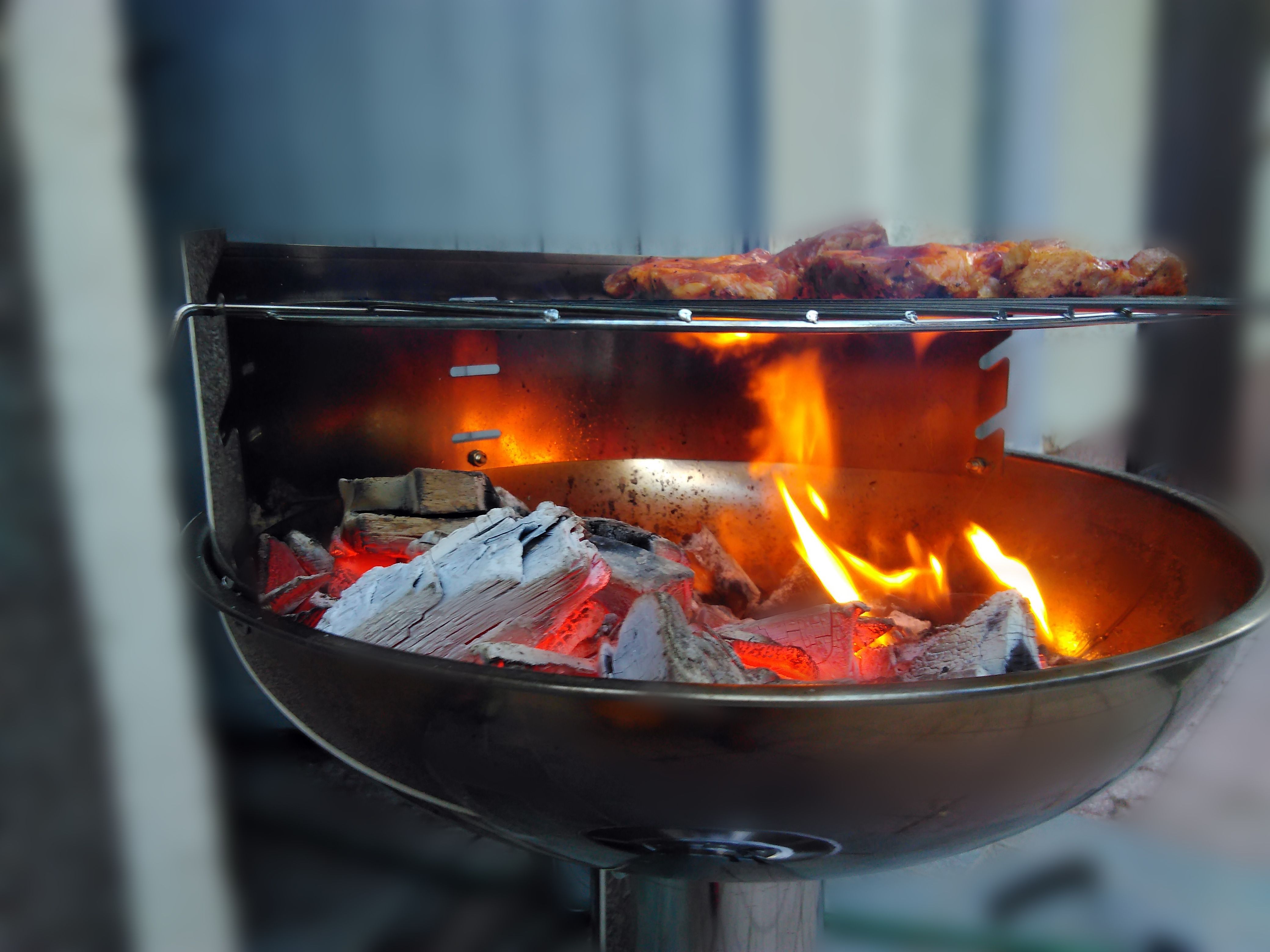 Ein Steak wird auf einem Grill angebraten, in dem Grill leuchtet eine hell rote Flamme