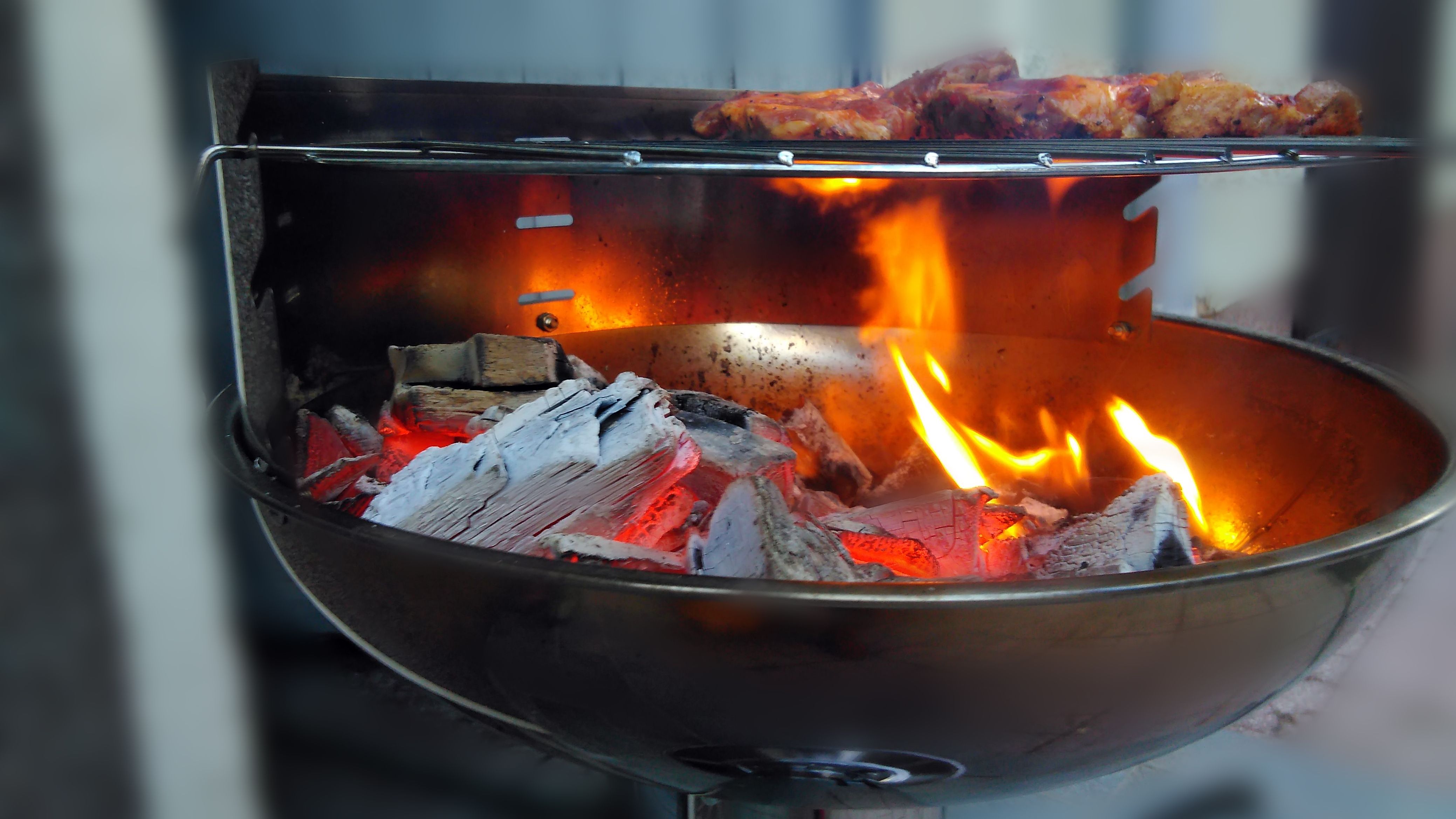 Ein Steak wird auf einem Grill angebraten, in dem Grill leuchtet eine hell rote Flamme